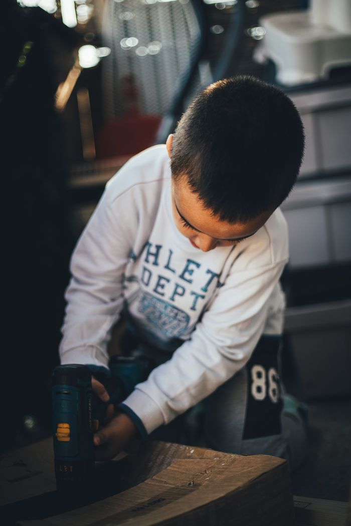 A young boy focused on a carpentry project using a power drill indoors.