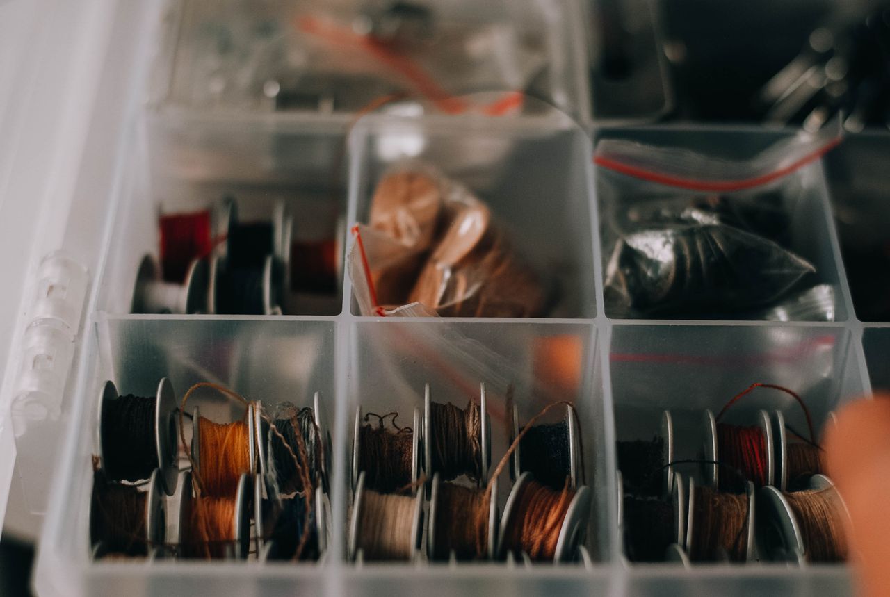 Close-up of assorted sewing threads in transparent organizer box for crafting and sewing projects.