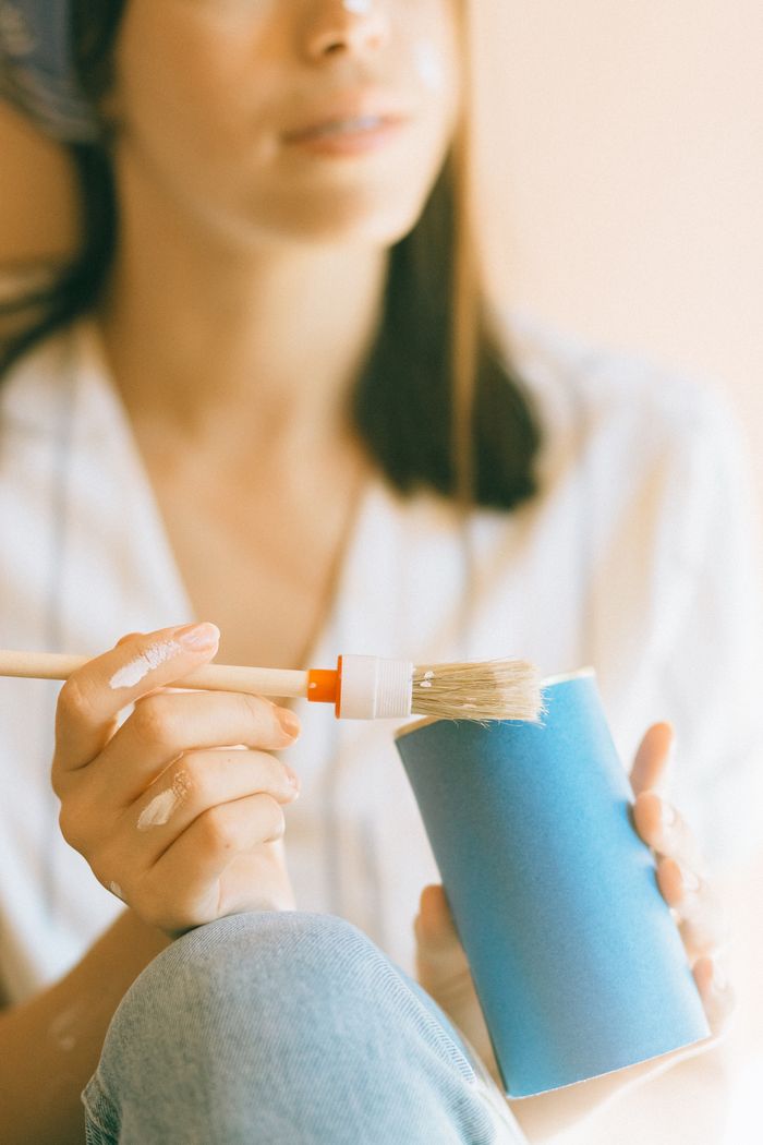Close-up of woman painting a blue cup indoors, focusing on DIY craft.